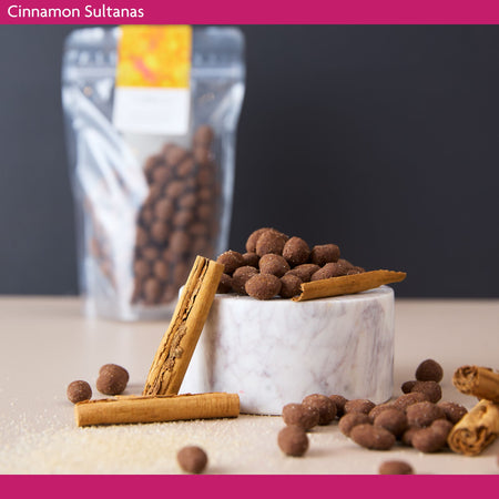 Cinnamon sultanas in milk chocolate with cinnamon sticks on a marble surface against a dark background