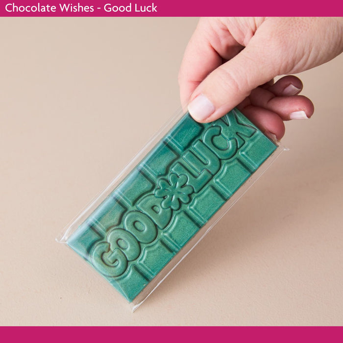Green chocolate bar with 'Good Luck' text held by a hand against a beige background