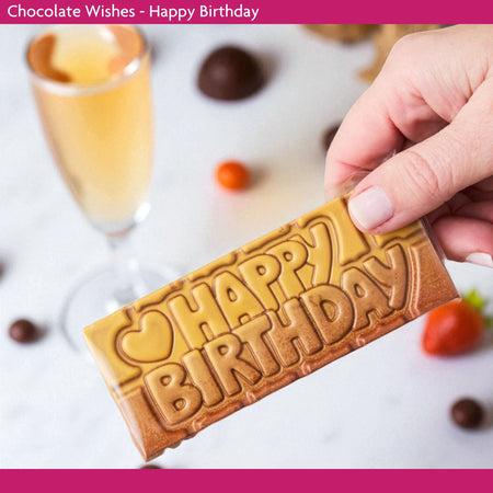 Chocolate bar with 'Happy Birthday' text held by a hand, with a glass of champagne in the background.