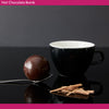 Hot chocolate bomb on a spoon with a black cup in the background
