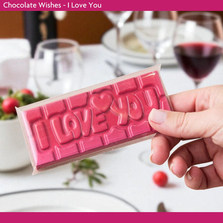 Chocolate bar with 'I LOVE YOU' text held by a hand, set against a romantic dinner background.
