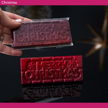 Red 'Merry Christmas' chocolate bar held by a hand with a dark background