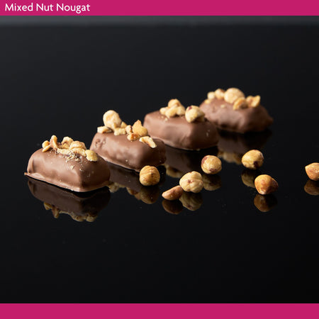 Chocolate-dipped mixed nut nougat on a black reflective surface