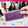 Purple chocolate bar with 'THANK YOU' text held by a hand, blurred office workshop background