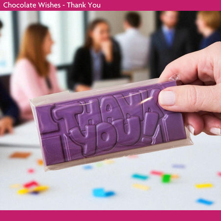 Purple chocolate bar with 'THANK YOU' text held by a hand, blurred office workshop background