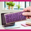Hand holding a purple chocolate bar with 'THANK YOU' text, blurred office background