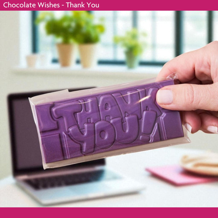 Hand holding a purple chocolate bar with 'THANK YOU' text, blurred office background
